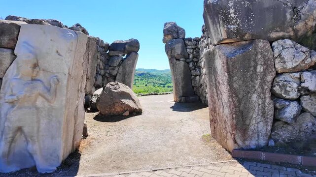 A relief of the Hittite Weather God stands beside cyclopean stone walls framing the ancient King's Gate at Hattusa.