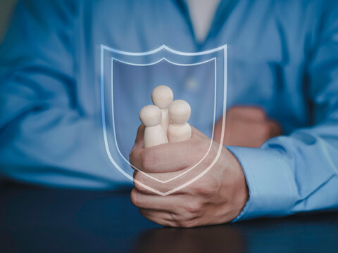 Life insurance, social security, health protection, financial safety and welfare planning for children and parents trust. Hands protecting wooden family figures with shield outline.