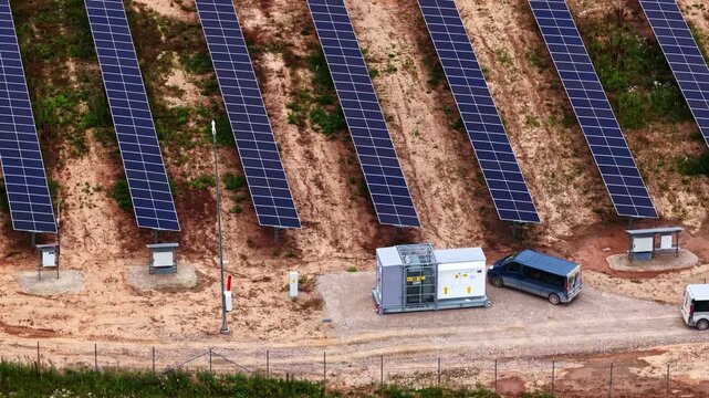 Aerial view of solar farm panels arranged in rows on a hillside with a small service building and a van parked nearby in Tume, Tukums Municipality, Latvia.