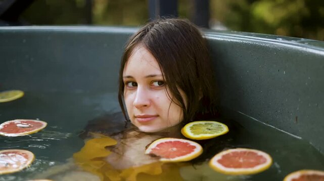 A beautiful model submerges gently in a dark green tub, surrounded by floating citrus slices. This serene girl enjoys a relaxing soak, embodying natural detox and spa treatments for glowing skin.