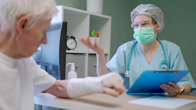 Elderly patient cooperates with rehabilitation specialist to plan faster recovery from arm fracture in clinical setting. Senior man trusts healer while discussing healing steps for restoring mobility.