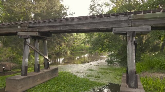 Aerial view of a historic wooden railway bridge crossing a calm stream surrounded by lush green trees and vegetation in Mareeba, Queensland, Australia.