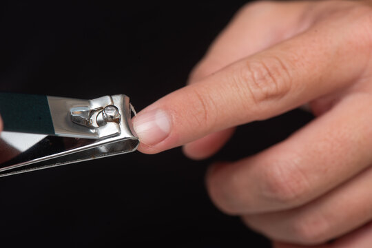 Close-up of a hand using stainless steel nail clippers to trim fingernails, showcasing the precision of the tool and the detail of the nail being clipped
