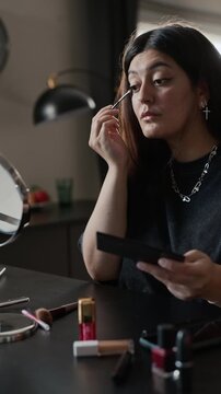Vertical shot of young woman applying eyeshadow with brush while looking in mirror. Low angle view is perfect for beauty tutorials, cosmetics advertising, and lifestyle vlogs