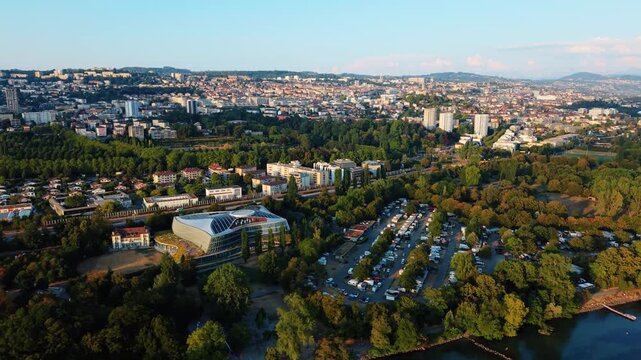 Aerial view of the International Olympic Committee headquarters surrounded by lush greenery, urban buildings, and a parking lot in Lausanne, Vaud, Switzerland.