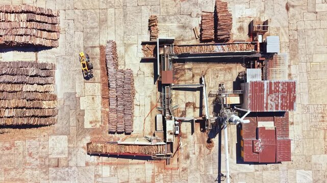 A wood processing site shows stacks of logs and machinery in use. Equipment moves materials around while workers prepare wood for various uses. This scene takes place in a busy area.