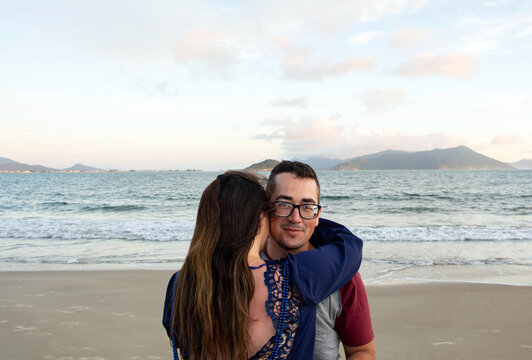 Young couple in love hugging on seashore and posing for a romantic portrait. Happy couple enjoying moment at beach. Man and woman in a peaceful coastal scene. Intimate moment. Love concept.