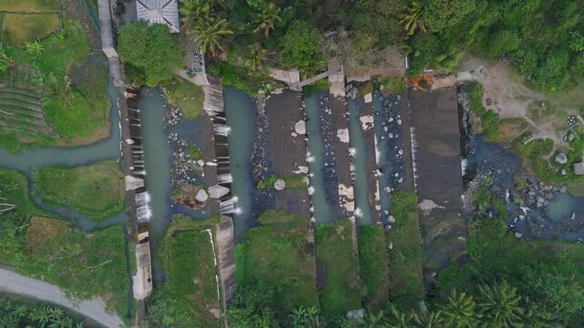 Aerial view of Grojogan Watu Purbo waterfall with cascading water over stone dams and lush green vegetation in Kecamatan Tempel, Daerah Istimewa Yogyakarta, Indonesia.