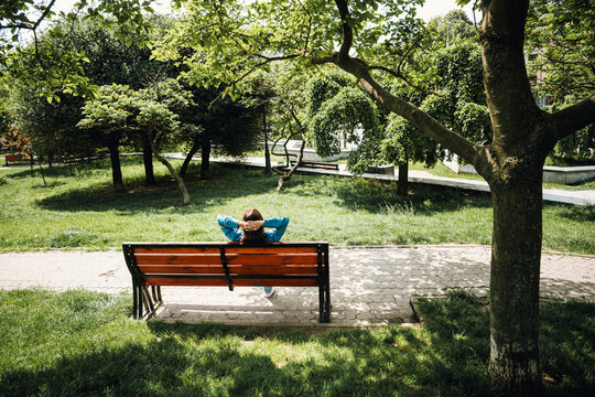 Woman relaxing on a bench in a leafy city park enjoying a peaceful afternoon under trees and dappled sunlight