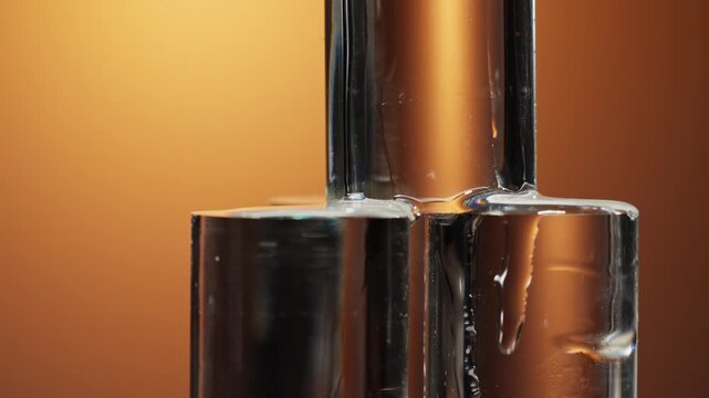 Close-up of transparent essence flowing through glass bottle against warm orange background