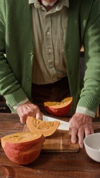 Vertical of senior man cutting fresh pumpkin on wooden board and sharing slice with senior Caucasian woman in kitchen. Footage perfect for senior lifestyle or healthy cooking campaigns