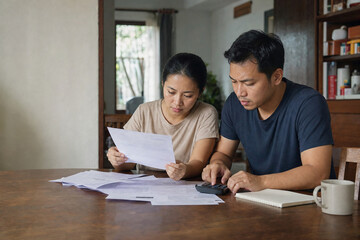 Obraz premium Asian couple reviewing household bills and calculating monthly expenses