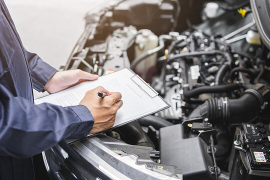 Auto check, car service shop concept. Automobile repairman writing job checklist on clipboard, mechanic checking engine to estimate repair machine, inspecting maintenance by engineer at vehicle garage