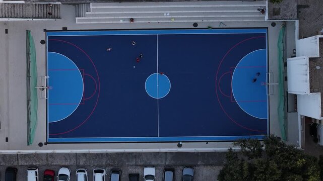 Aerial view of a blue outdoor sports court with people playing and a nearby parking lot in Cascais, Portugal.