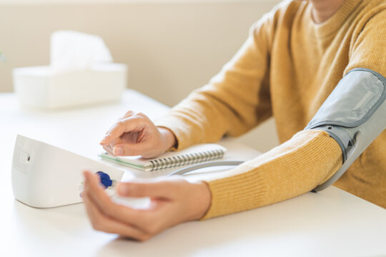 Hypotension problem, close up hand of  young woman check pulse, measure high blood pressure heart rate, holding digital pressure monitor, making self on arm, cuff on sofa at home. Healthcare medical.