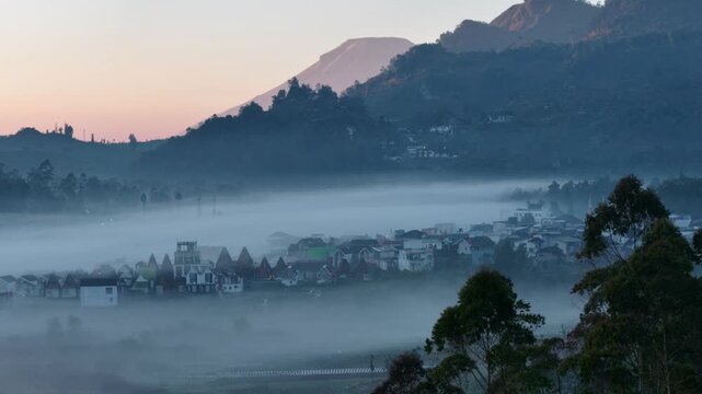 Aerial view of Dieng Plateau with morning mist, volcanic mountains, and village houses in Indonesia.