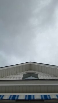 Vertical timelapse view of quick moving clouds in an overcast sky above the pointed eve of a house