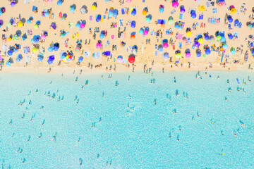 Obraz premium Aerial drone view of people relaxing on a white sand beach under colorful umbrellas. Bright sunny summer vacation scene by turquoise crystal clear sea water.