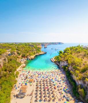 Aerial drone view of a beach with colorful umbrellas and people relaxing. Turquoise crystal clear sea water and white sand during a bright sunny summer vacation.