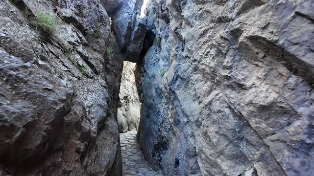 A narrow stone alleyway winds between towering rock walls beneath a suspended boulder at the ancient site of Hattusa.