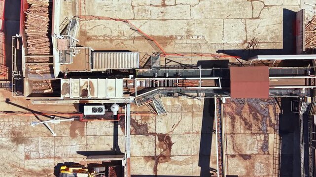A wood processing area with large machines and stacks of logs. The location is an industrial site where logs are processed. It is daytime and the site is busy.