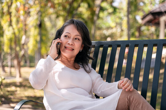Asian Adult Woman Relaxing on Bench Talking on Phone in Park Sunny Day Leisure Mobile Communication Outdoors Conversation