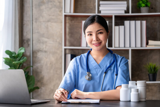 Smiling Asian Female Doctor at Desk with Laptop and Medicine Bottles in Office Setting Professional Healthcare and Telemedicine Concept for Health and Wellness
