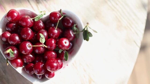Top down close view of heart shaped bowl filled with glossy ripe cherries on pale wooden surface, bright sunlight and fresh negative space for caption layout, with berry, background, summer, juicy