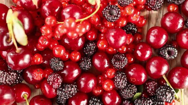 Overhead closeup of mixed red berries and cherries with shifting focus revealing glossy skins, ripe color, textured dark fruit, and natural wooden surface detail