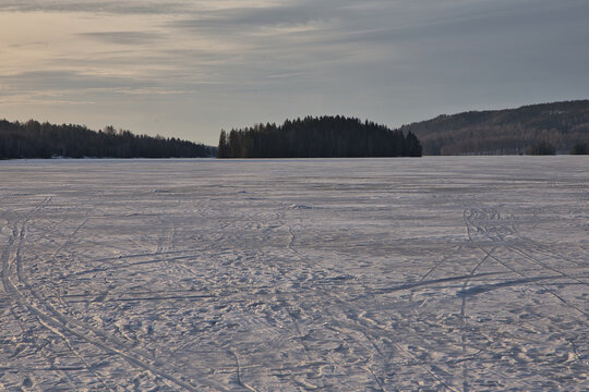 Winter sunset over frozen Lake arr in Dalsland, Sweden; golden sun rays shining behind an old stone ruin on a snowy shore with a peaceful, scenic wilderness atmosphere