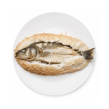 Lubina a la Sal, ganze spanische Wolfsbarschzubereitung in einer aromatischen Salzkruste, auf wei&szlig;em Teller pr&auml;sentiert und freigestellt aus der Vogelperspektive fotografiert.