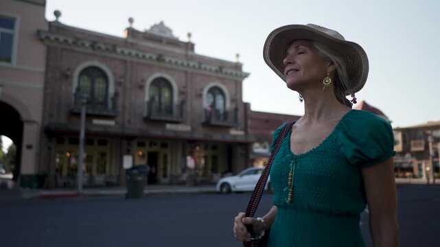 A happy woman walks by the Sebastiani Theater in Sonoma, exploring the area as a tourist on a sunny morning.