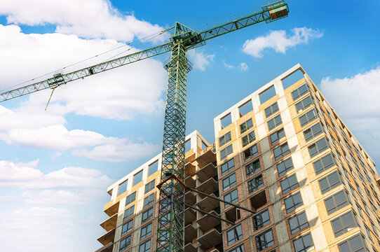 Modern residential building under construction with tower crane and blue sky with white clouds