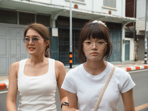 Two young Asian women friends walking together on an urban street during daytime.