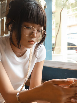 Young Asian woman with stylish glasses intently focused on her smartphone screen indoors.