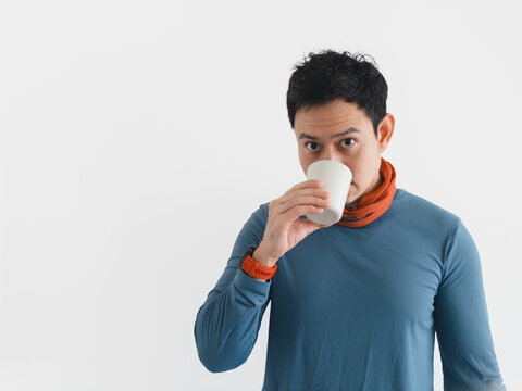 Young Asian man drinking from a white cup, looking at camera with neutral expression.