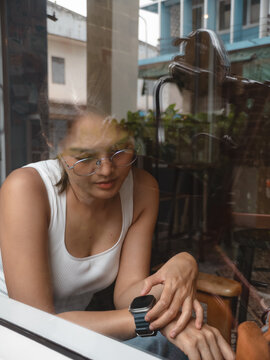 Young Asian Woman Checking Her Smartwatch While Sitting Inside a Cafe with Window Reflections
