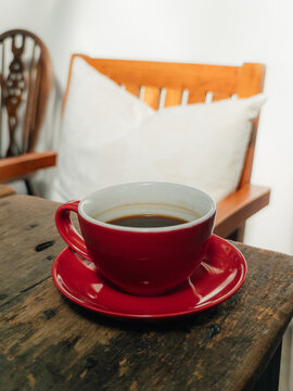 Close-up of a vibrant red coffee cup with black coffee on a rustic wooden table.