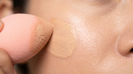 Fototapeta premium Close-up of a person using a pink makeup sponge to apply liquid foundation to their cheek, ad social media download thambnail poster web template event festival 2026 2027 2028