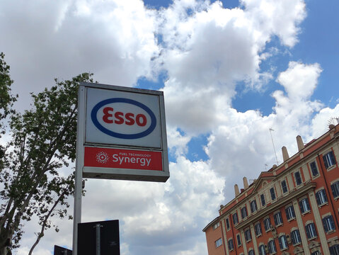 Rome, Italy - May 17, 2026: Esso fuel station sign with Synergy branding against a backdrop of clouds and a colorful building in an urban setting