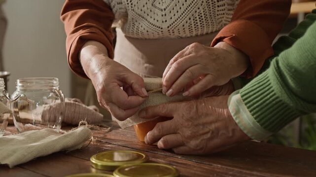 Senior Caucasian couple wrapping homemade jar with burlap as camera tilts up to smiling woman. Clip is perfect for retirement lifestyle promos and organic food marketing campaigns