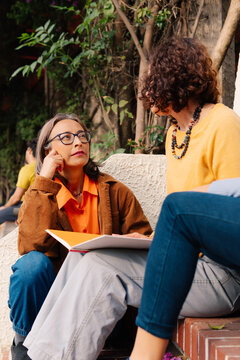 Adult women conversing while sitting on stairs.