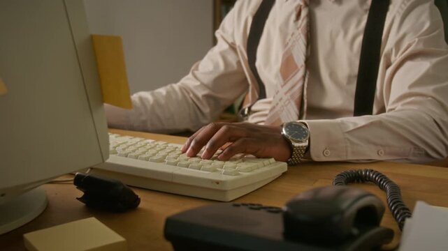 Midsection shot of African American man typing on retro computer keyboard in vintage office. Clip is ideal for nostalgic corporate training videos or historical business presentations