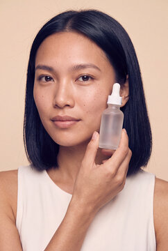 Woman holding frosted glass serum bottle near face for skincare routine portrait and cosmetic product promotion background