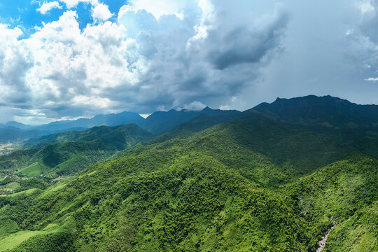 Lush green hills cover the foreground leading toward a coastal city skyline and blue ocean waters under a bright sunny sky during a peaceful afternoon
