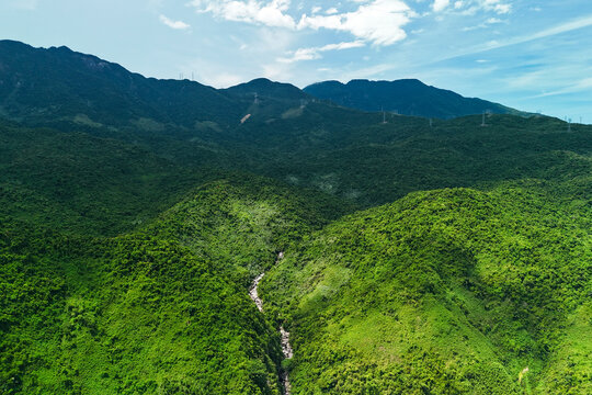 Green mountain slopes surround a small winding river with several tents pitched along the bank in the middle of a lush tropical wilderness area during the day
