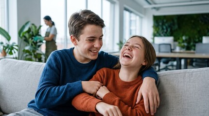 Fototapeta premium Joyful teenage siblings share a laugh while relaxing on a couch in a modern office setting