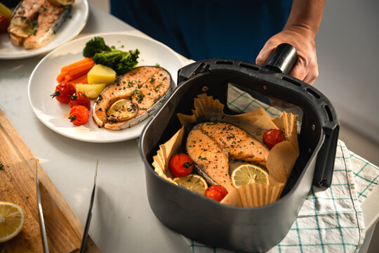 Air Fryer Cooking with Salmon Steaks, Lemon and Roasted Tomatoes beside a Healthy Plated Meal of Fish, Broccoli, Carrots and Potatoes in a Home Kitchen