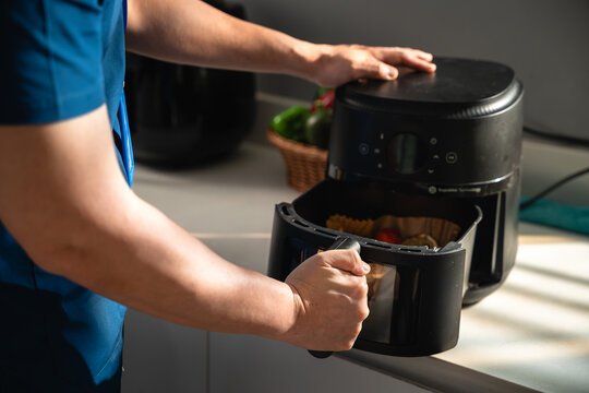 Male Caregiver Using an Air Fryer to Prepare a Healthy Salmon Meal in a Bright Home Kitchen while Opening the Cooking Basket on the Countertop