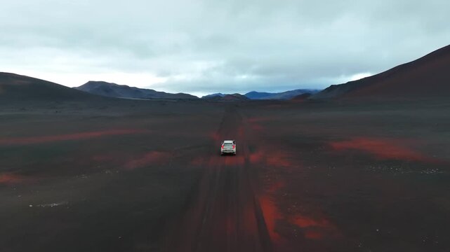 Aerial view of a car driving on a remote volcanic dirt road through the vast Askja caldera landscape under a cloudy sky in Reykjahlid, Thingeyjarsveit, Iceland.